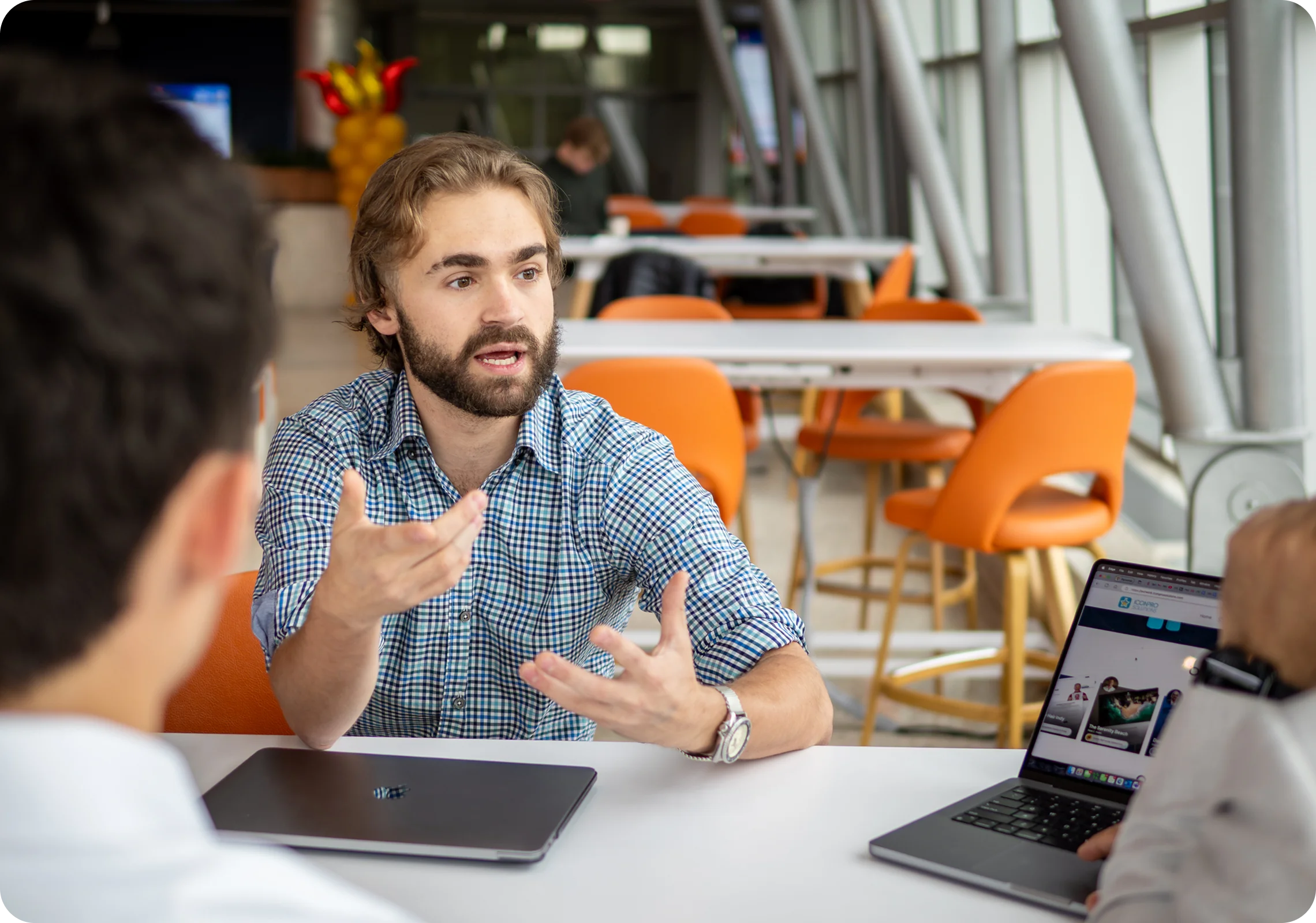 A man explaining something with both hands at a table with laptops
