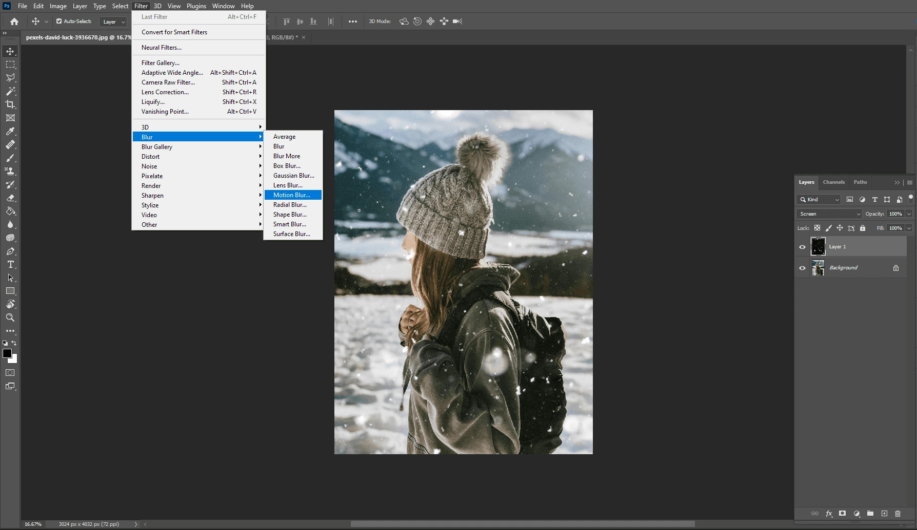 Photoshop Filter menu open at Blur, Motion Blur, over a photo of a person in a knit hat in the snow