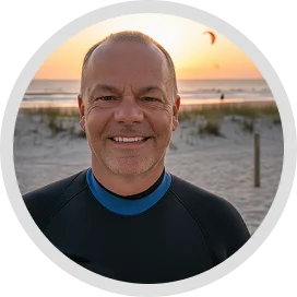 testimonials A man in a black wetsuit with a blue collar, smiling at the camera, with a beach and sunset in the background,