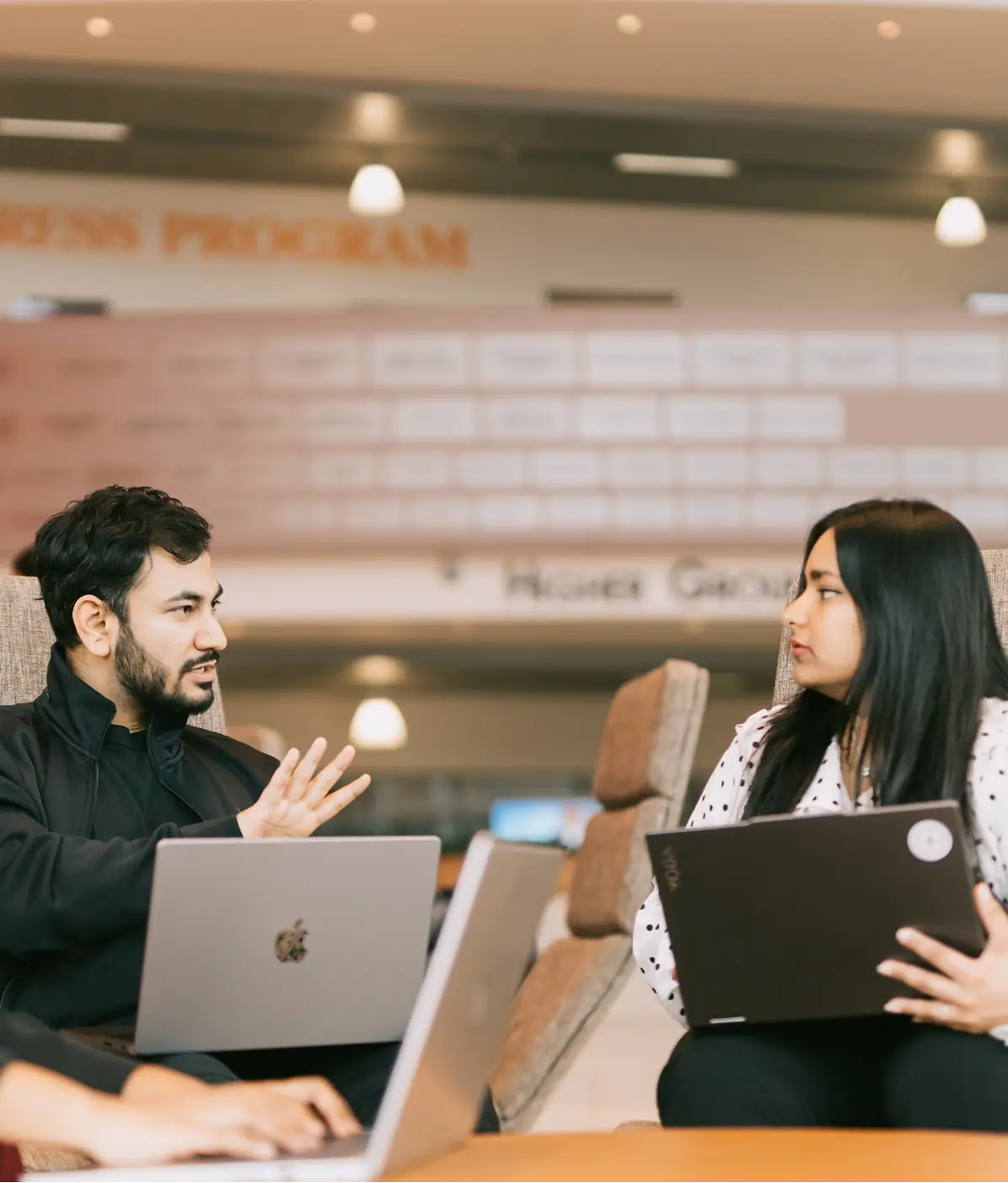 Two people talking across a lounge table, each with a laptop open