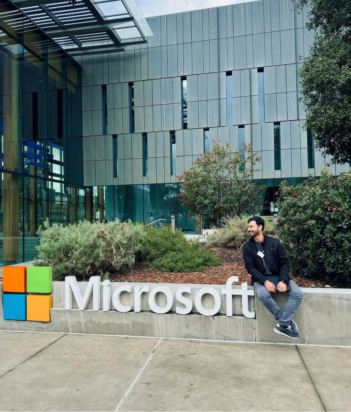 A man sitting on a large Microsoft sign outside a glass office building