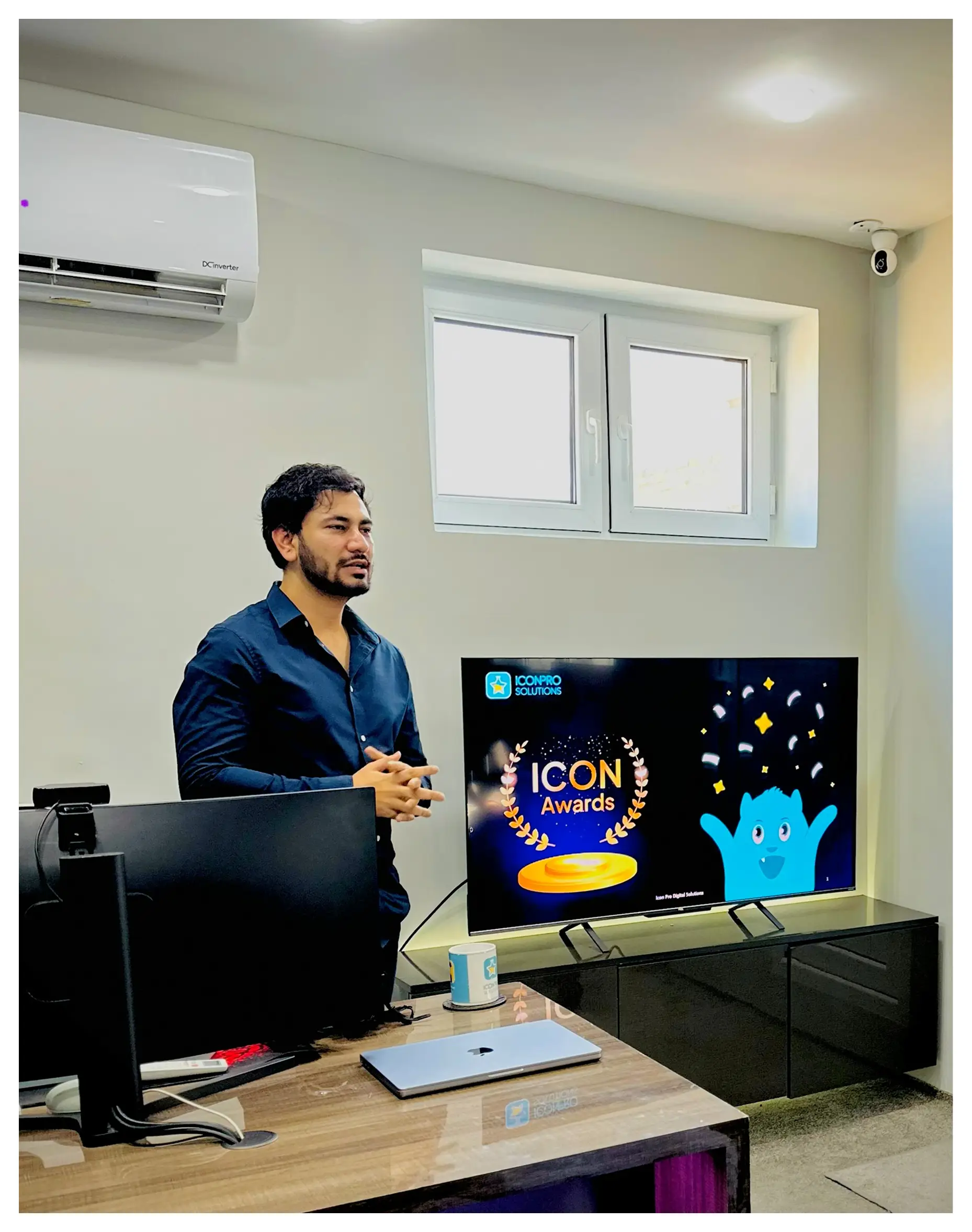 contact-us A man in a blue shirt standing in front of a TV screen displaying the 'ICON Awards' logo, with a computer monitor
