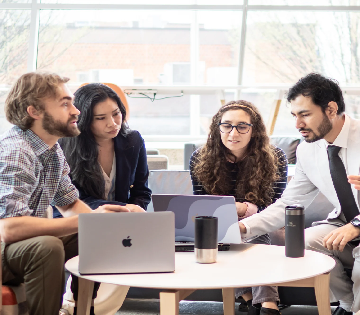 Four people gathered around a laptop at a round table, discussing work