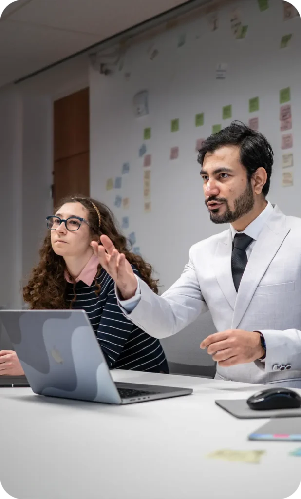 Two people sitting at a table with a laptop and mouse in front of them, engaged in a meeting
